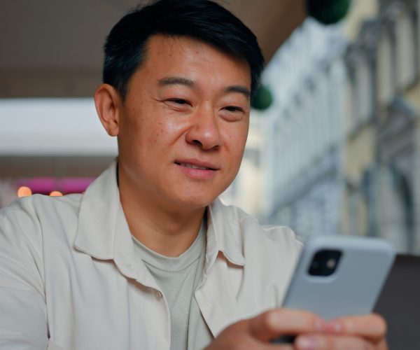 Close-up happy asian man holding mobile phone browsing social network male tourist booking ticket using smartphone sends email message communicates in internet chat making purchase in online store Close-up happy asian man holding mobile phone browsing social network male tourist booking ticket using smartphone sends email message communicates in internet chat making purchase in online store. High quality 4k footage